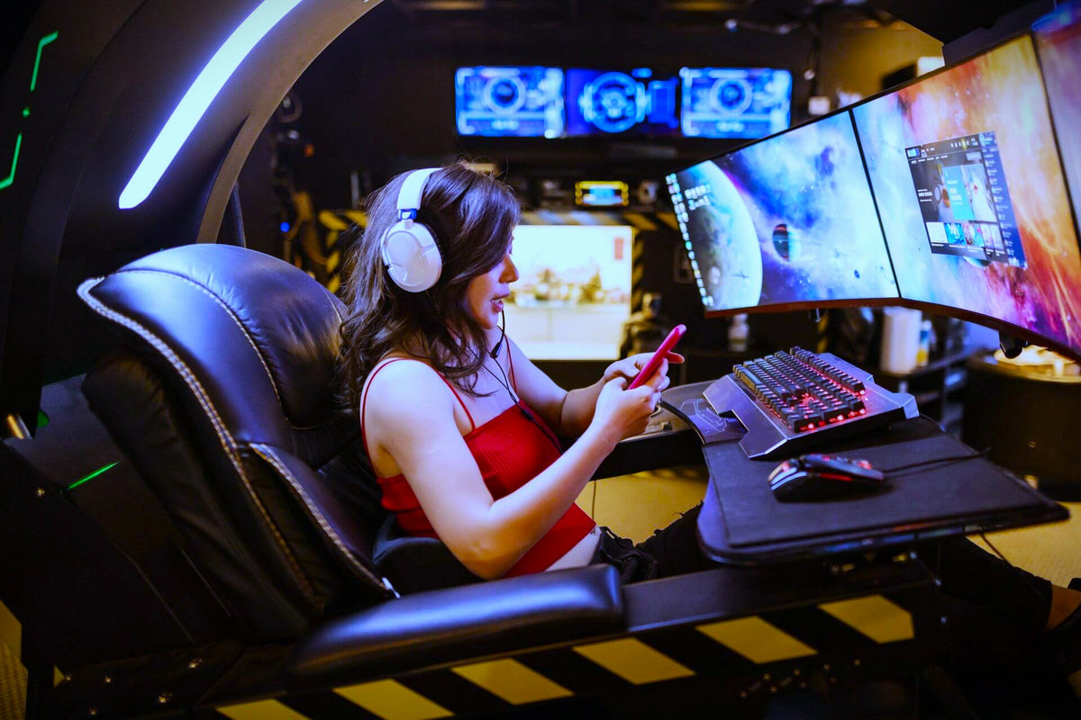 Gamer with headphones on her phone in a Green Beast Gaming battle station with curved ultrawide monitors